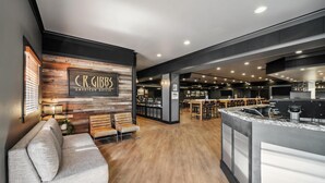 A modern restaurant interior with a wooden accent wall, a bar area, and a seating section with a sofa and chairs. - Best Western Plus Hilltop Inn (Redding)