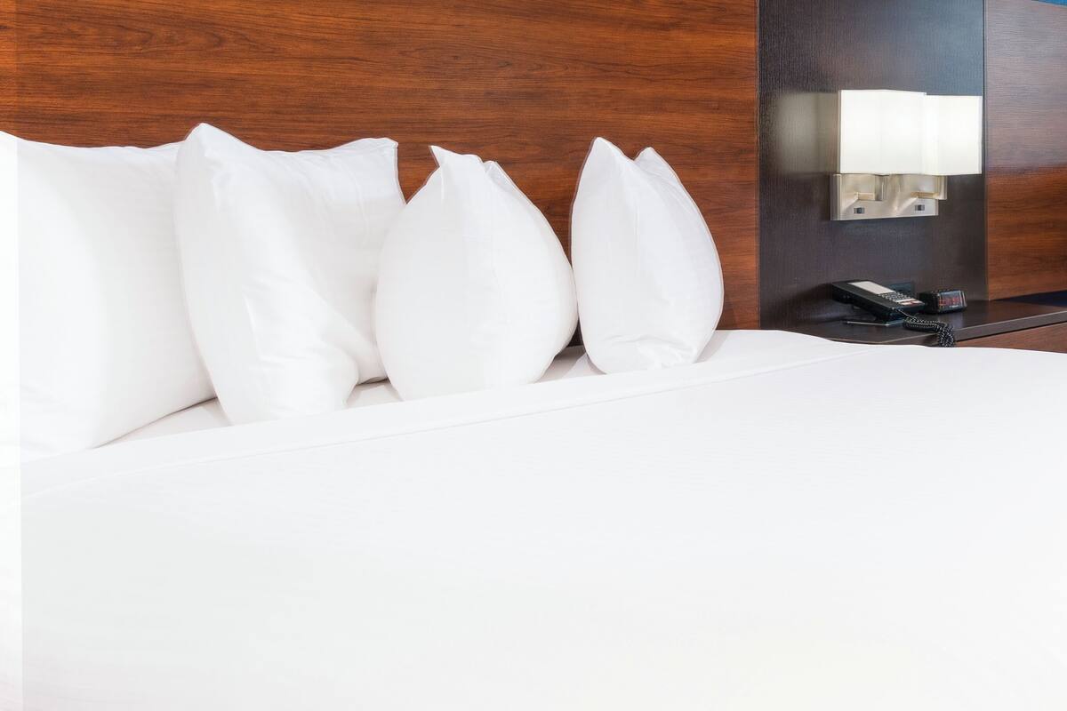 Un lit bien fait, avec du linge de lit et des oreillers blancs, un téléphone sur la table de chevet et un luminaire fixé au mur.