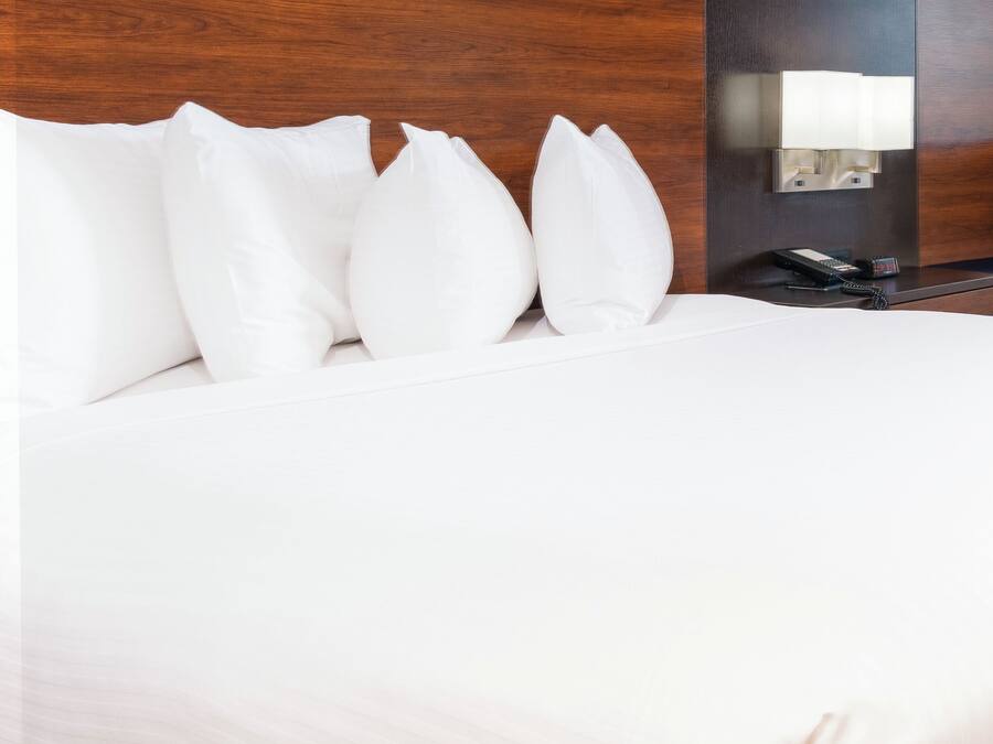 A neatly made bed with white bedding and pillows, a bedside telephone, and a wall-mounted light fixture.