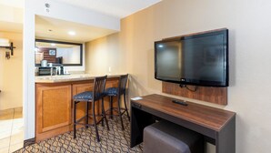 Une chambre d’hôtel compacte dotée d’une kitchenette, d’un téléviseur à écran plat fixé au mur, d’un petit bureau et de deux tabourets de bar.