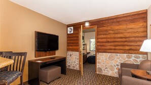Une chambre d’hôtel avec un mur en bois, une télévision, un bureau, une chaise et un canapé.