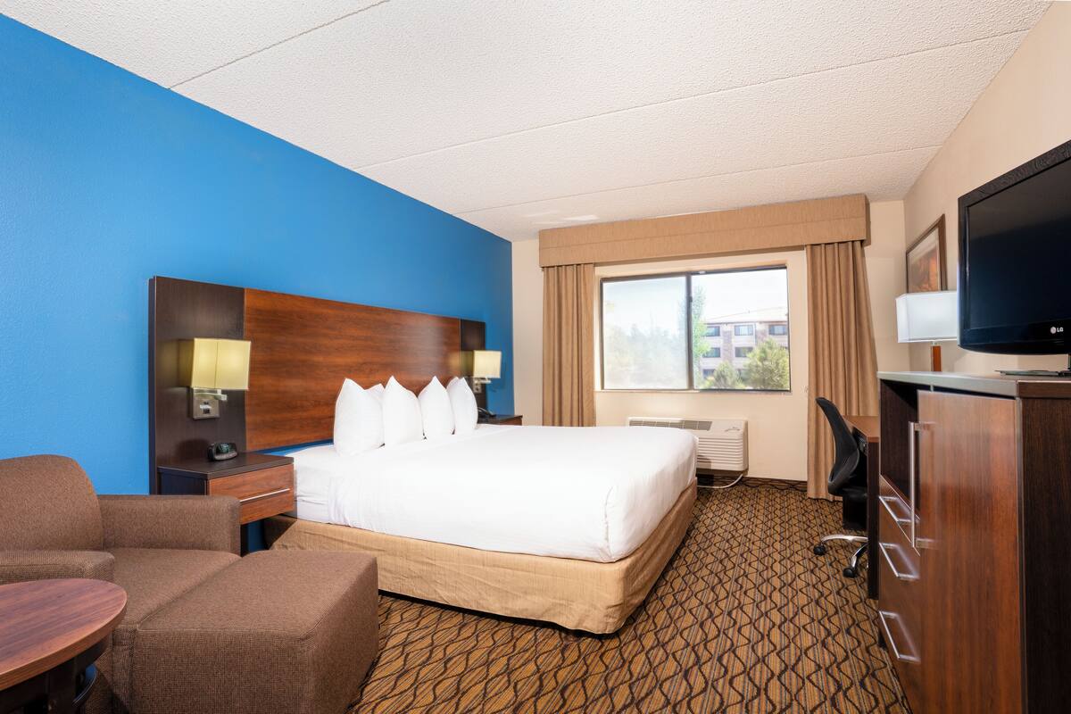 Une chambre d’hôtel avec un grand lit, un bureau, une chaise, une télévision et une fenêtre avec des rideaux.