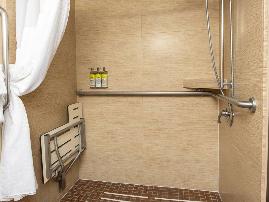 A shower area with a showerhead, curtain, and a shelf with toiletries.