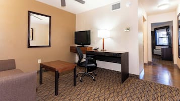 A hotel room with a desk, chair, television, and a mirror.