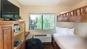 Une chambre d’hôtel équipée d’un lit, d’une télévision, d’une fenêtre avec stores, d’une tête de lit en bois et d’un climatiseur fixé au mur.