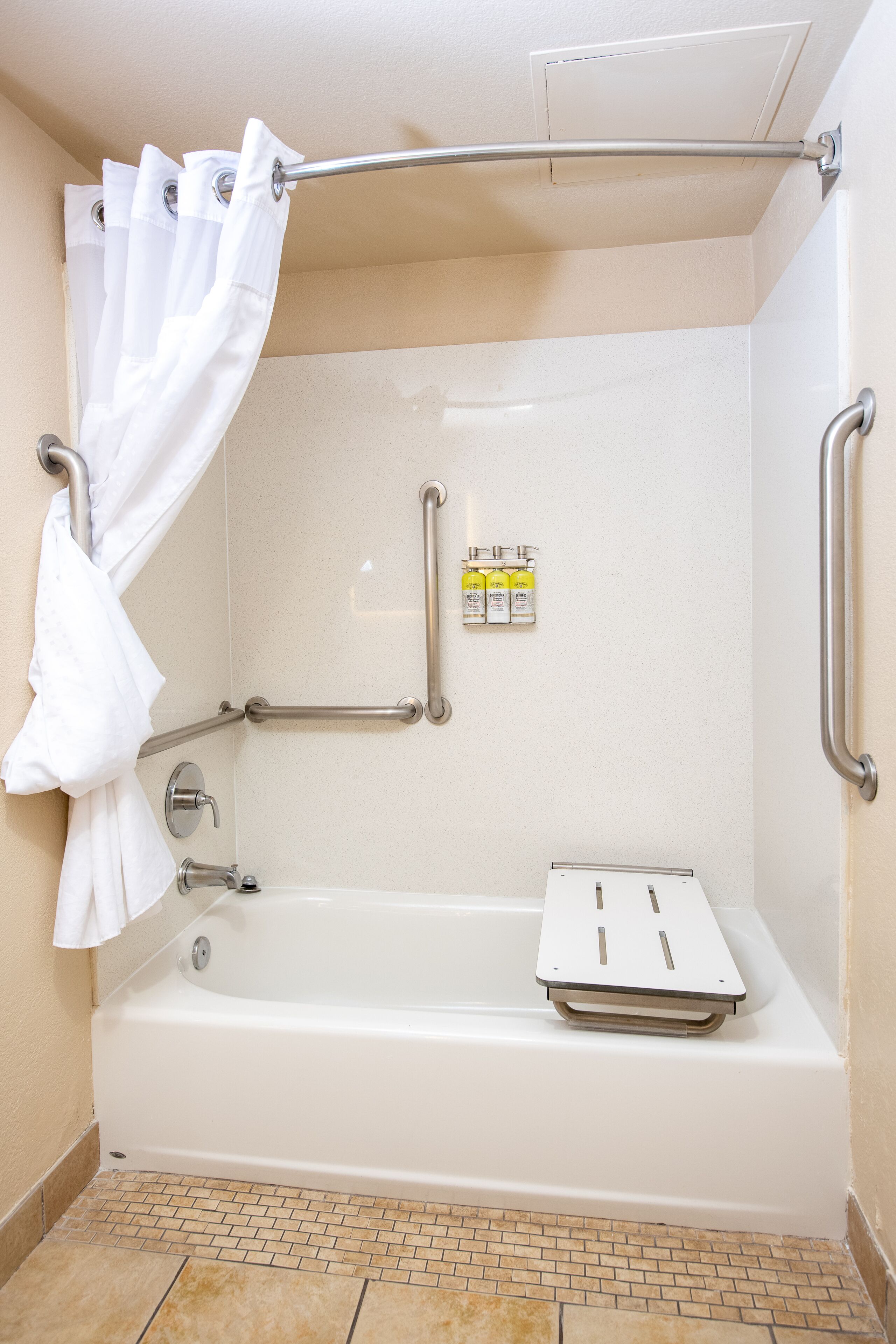 Une salle de bain avec une baignoire blanche, des barres d’appui, un rideau de douche et un distributeur de gel hydroalcoolique.
