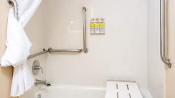 A bathroom with a white bathtub, grab bars, a shower curtain, and a hand sanitizer dispenser.