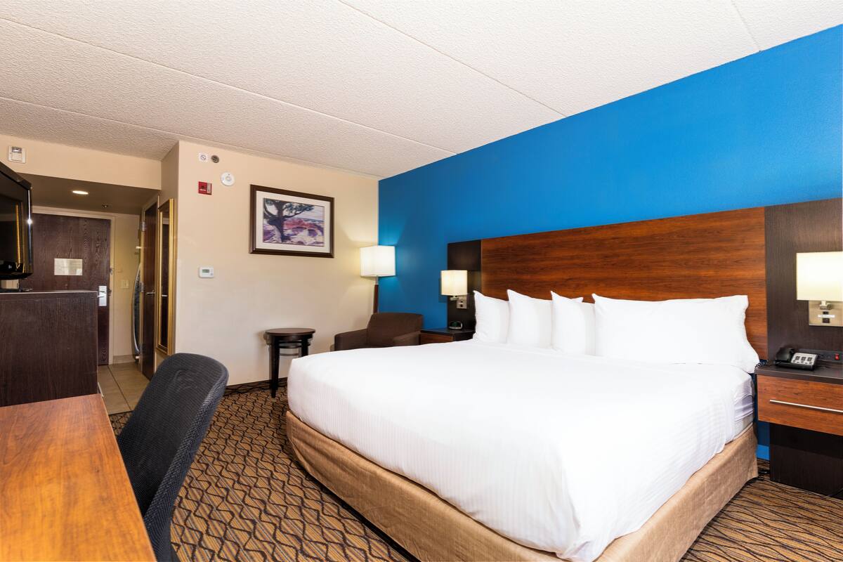 Une chambre d’hôtel avec un grand lit, un bureau, une chaise, une table de chevet et une lampe fixée au mur.