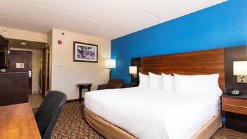 A hotel room with a large bed, a desk, a chair, a nightstand, and a wall-mounted lamp.