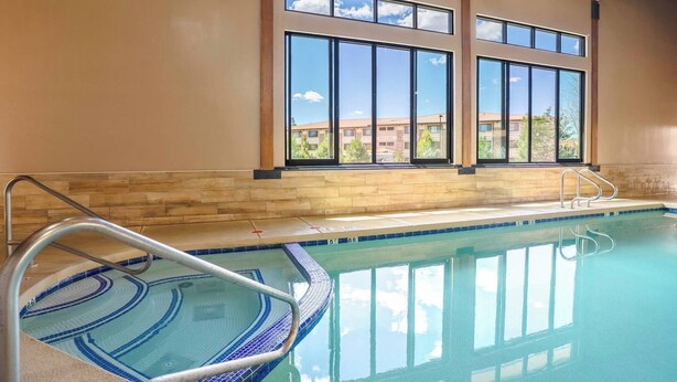 Une piscine intérieure avec de grandes baies vitrées, un sol carrelé et un escalier métallique pour y accéder.