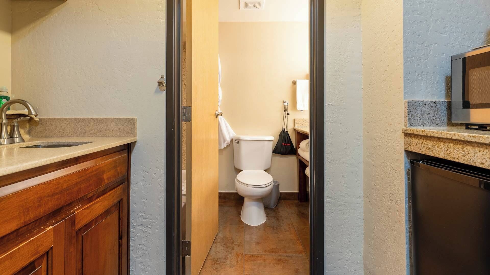 Un couloir étroit mène à une salle de bain équipée de toilettes, d’un lavabo et d’un petit meuble de rangement.