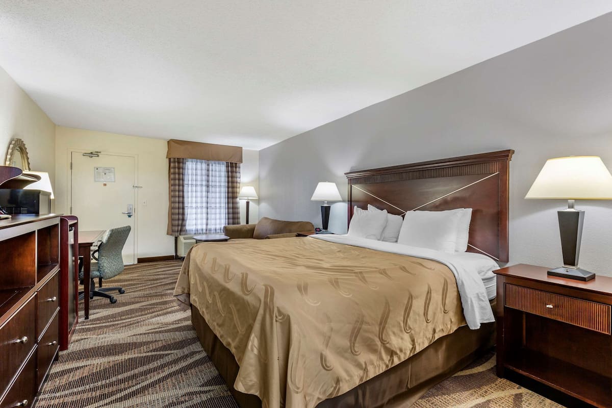 A hotel room with a large bed, a desk with a chair, a dresser, and two bedside lamps.