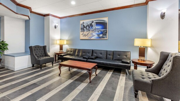 A lobby with a black leather sofa, a wooden coffee table, and two armchairs. There are two lamps on side tables and a painting on the wall. - Quality Inn Windsor Mill - Baltimore (Windsor Mill)