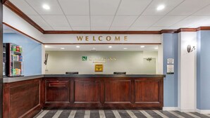A reception desk with a "WELCOME" sign above it, a framed logo of "Quality Inn by Choice Hotels," and a vending machine to the left. - Quality Inn Windsor Mill - Baltimore (Windsor Mill)