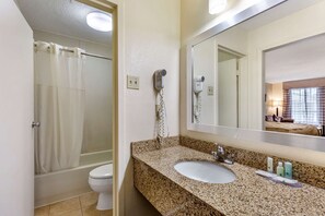 A bathroom with a shower, toilet, sink, and a hairdryer mounted on the wall.