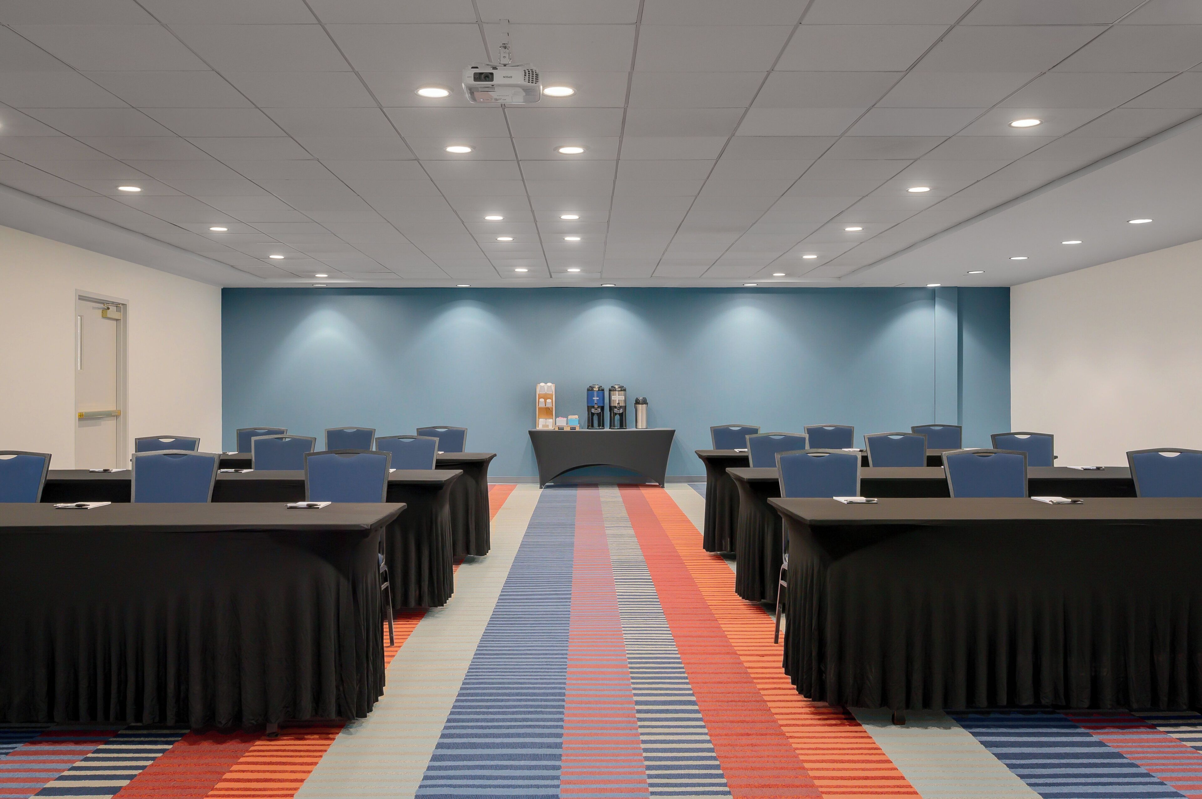 A conference room with a long table, chairs, a podium, and a carpeted floor.