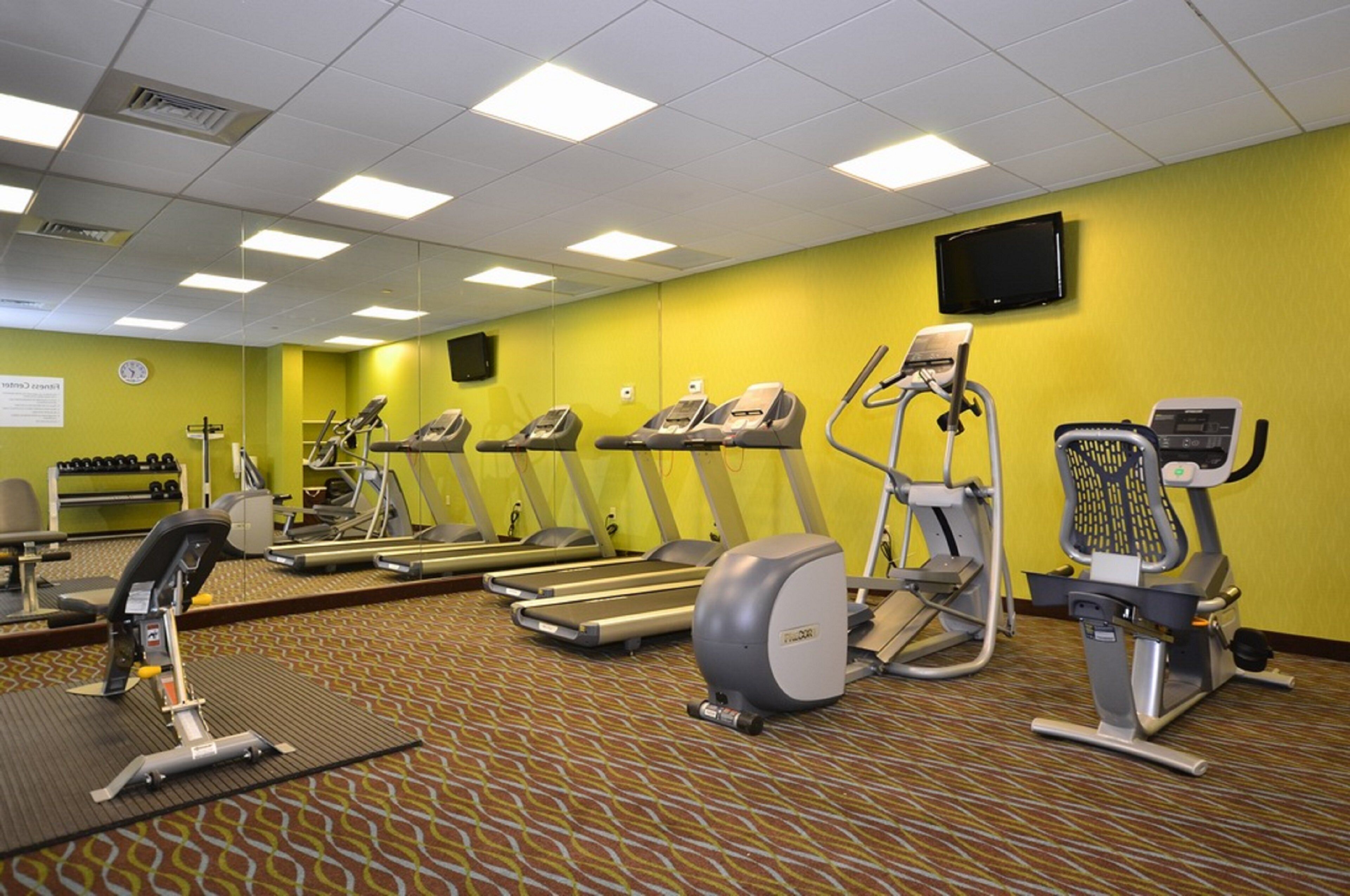 Un gimnasio equipado con cintas de correr, elípticas y un espejo grande.