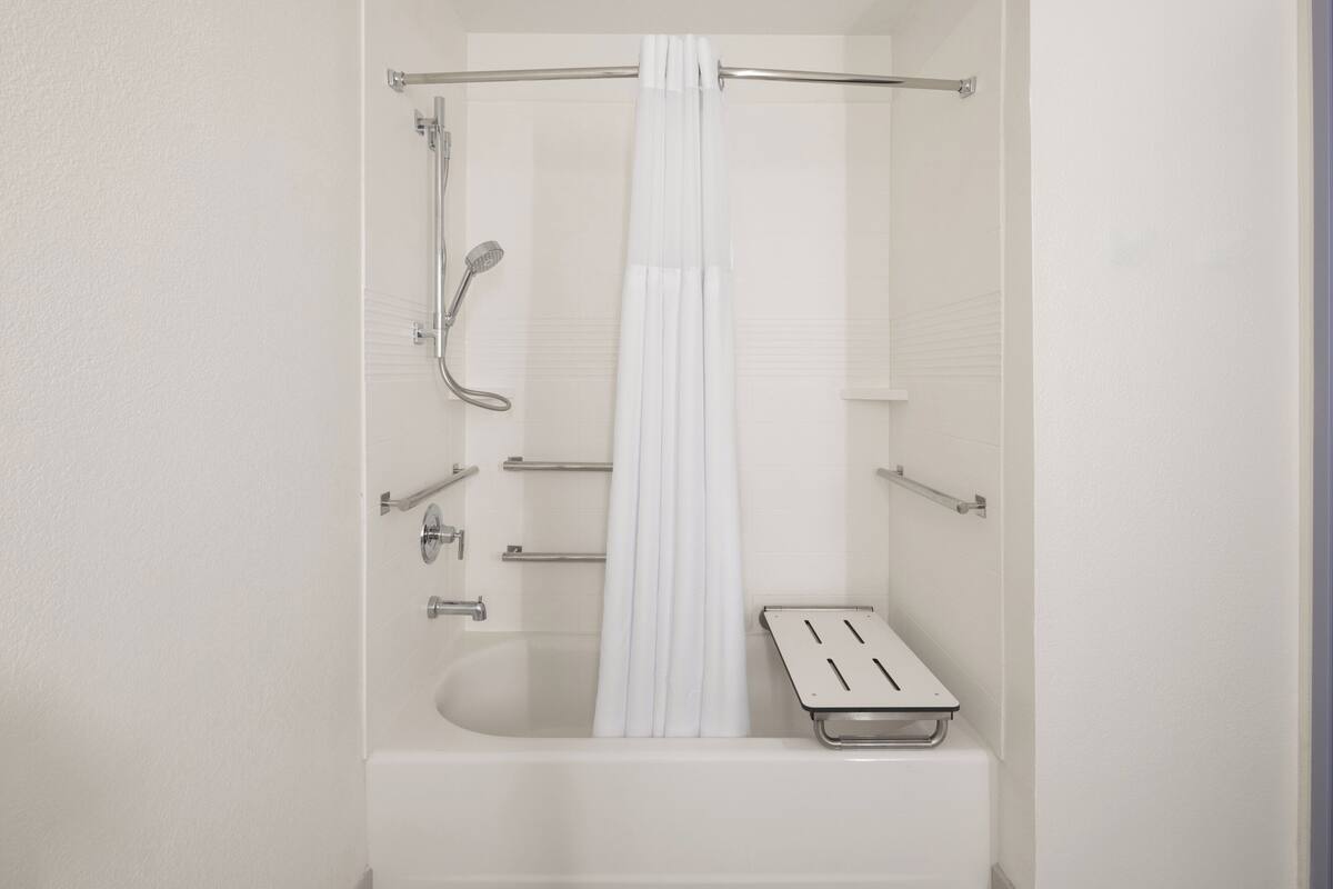 Une salle de bain moderne équipée d’une baignoire, d’une douche et de barres d’appui.
