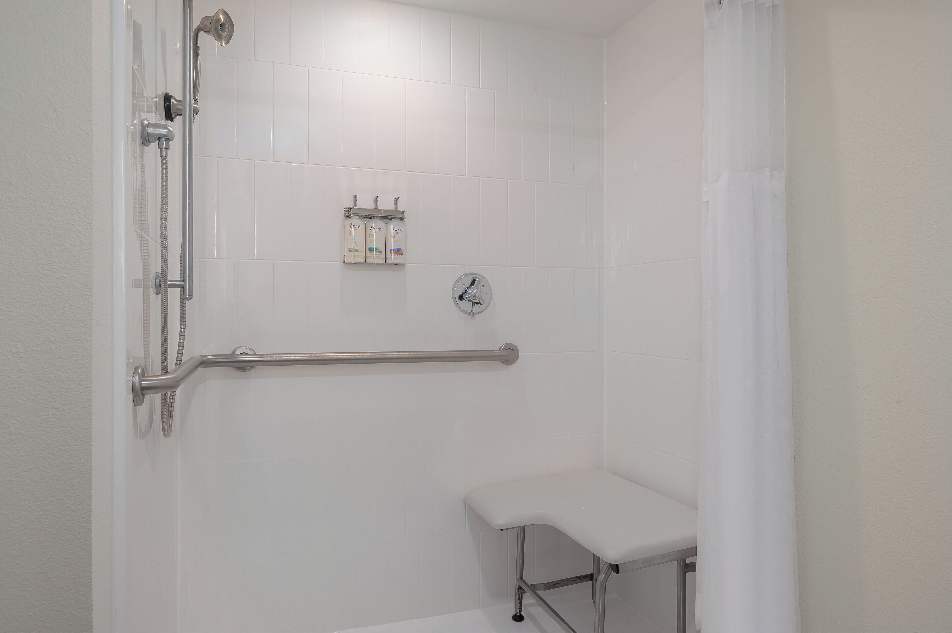 Un espacio de ducha con barra de apoyo, cabezal de ducha manual y grifo manual.