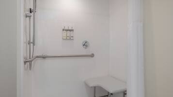 Un espacio de ducha con barra de apoyo, cabezal de ducha manual y grifo manual.