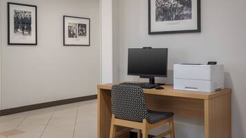 Een werkplek met een bureau, computer, printer en twee ingelijste foto's aan de muur.