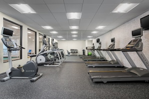 Une salle de sport équipée de tapis de course, de vélos elliptiques et d’une zone avec des bancs de musculation.