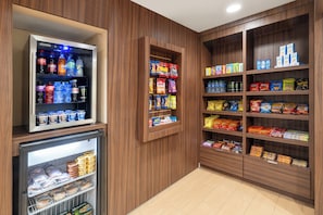 Un espace réfrigéré contenant des boissons et des en-cas, des étagères en bois où sont exposés des produits emballés, et un sol carrelé.