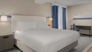 A hotel room with a large bed, a desk, a chair, a lamp, and a nightstand.