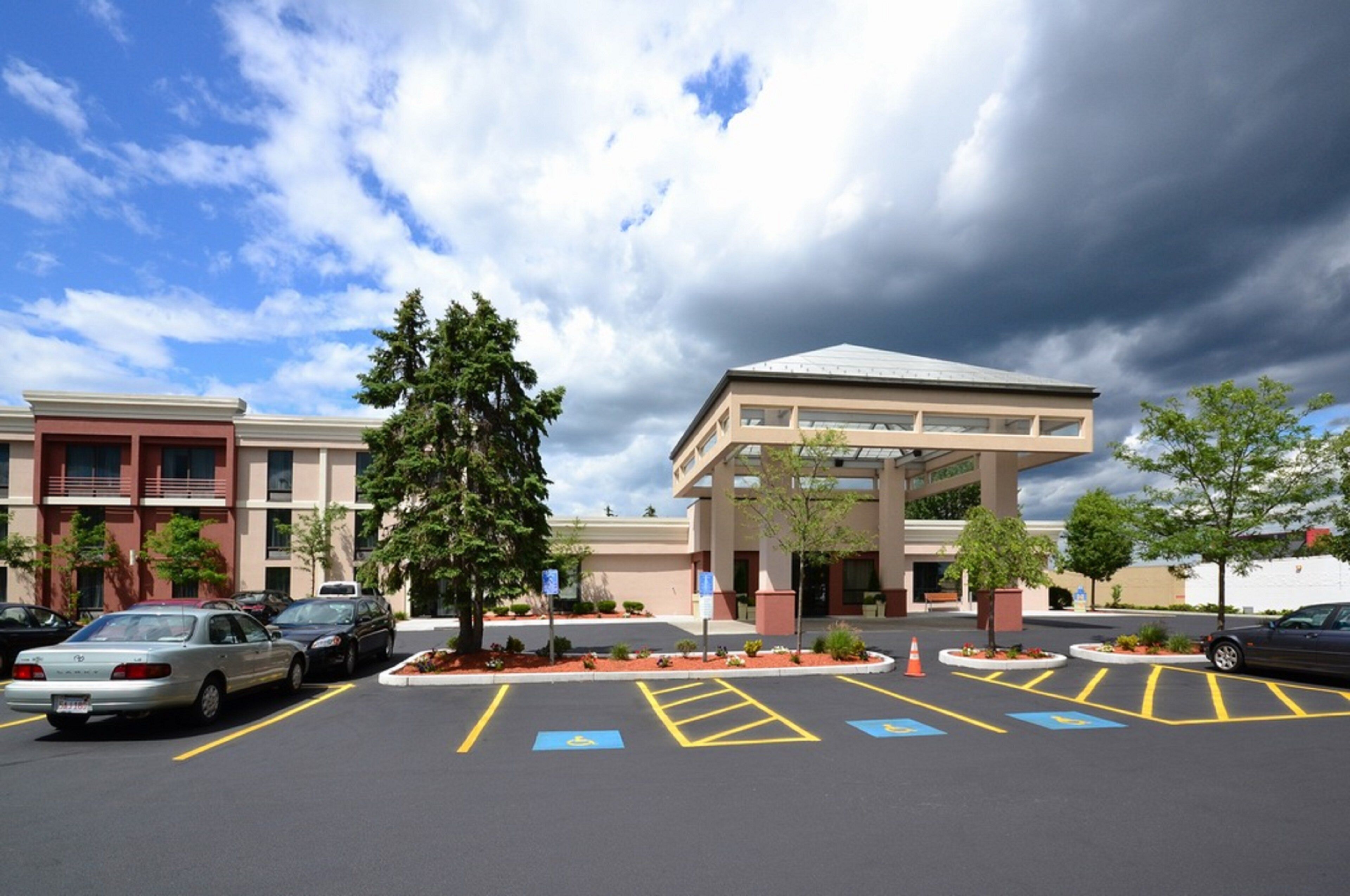 A parking lot with handicapped accessible spaces, a building with a flat roof, and a tree in the foreground.