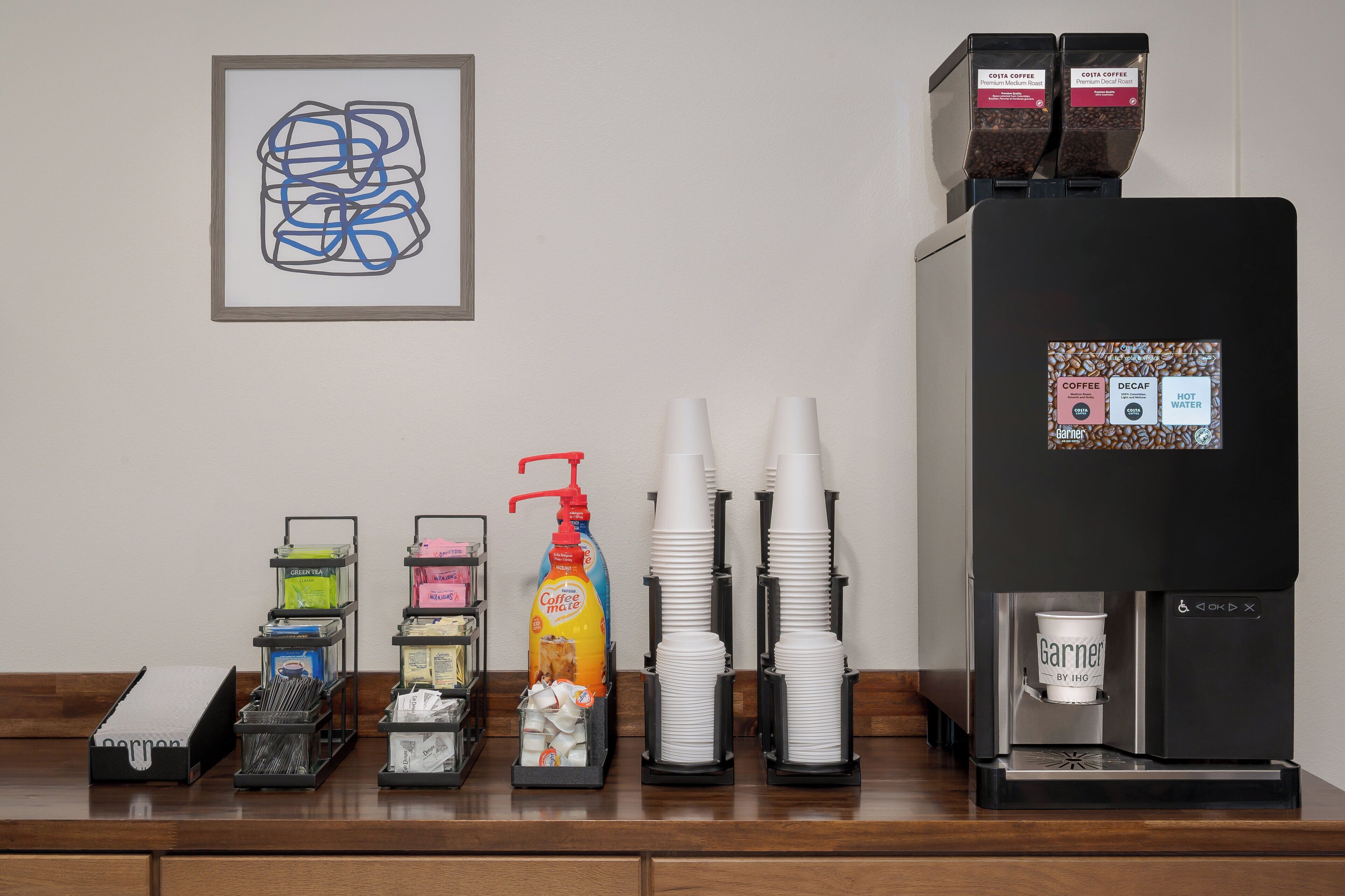 A coffee station with a coffee machine, cups, and various coffee and tea dispensers.