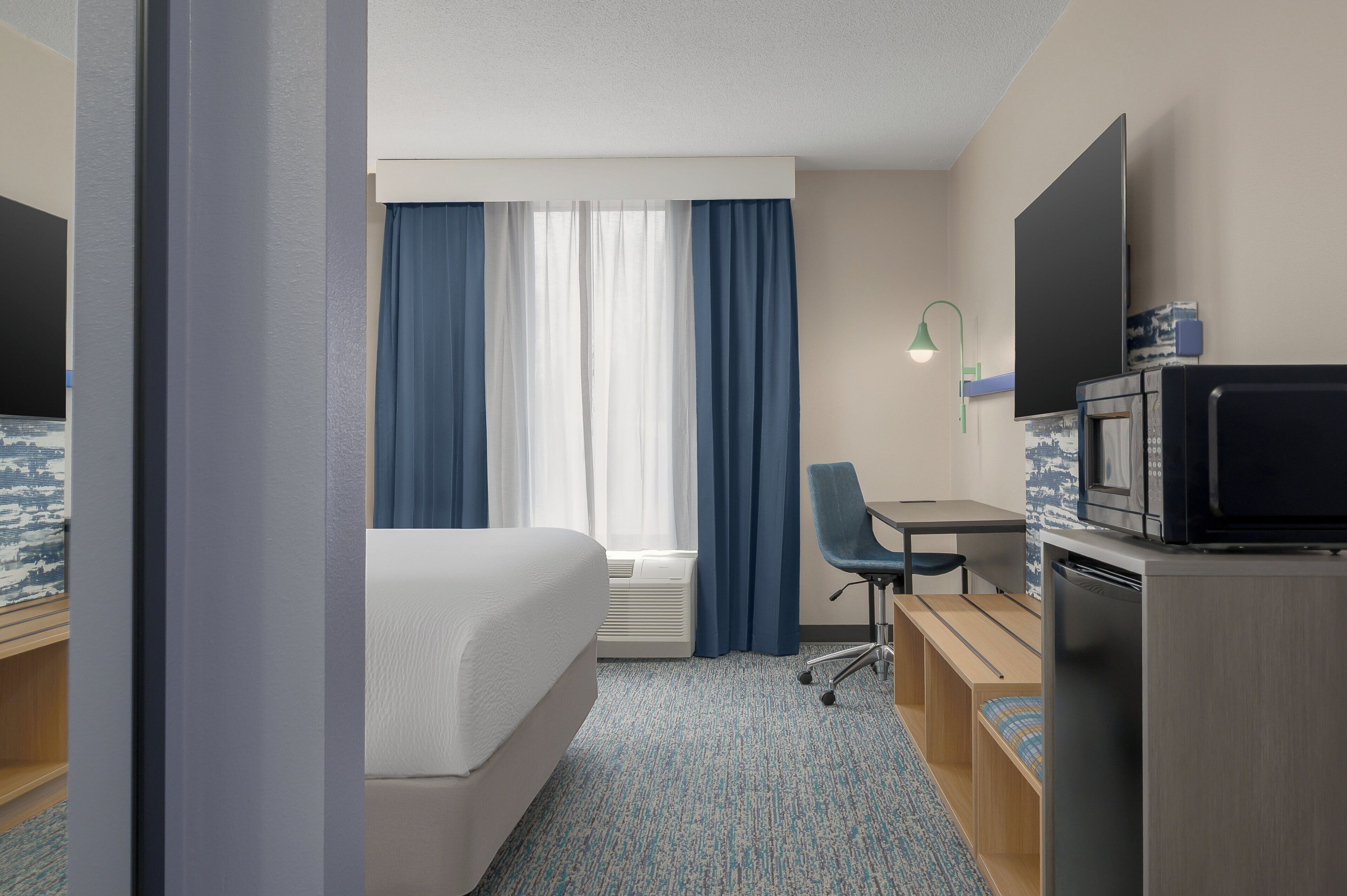 Una habitación de hotel con cama, escritorio, silla, televisor y microondas.