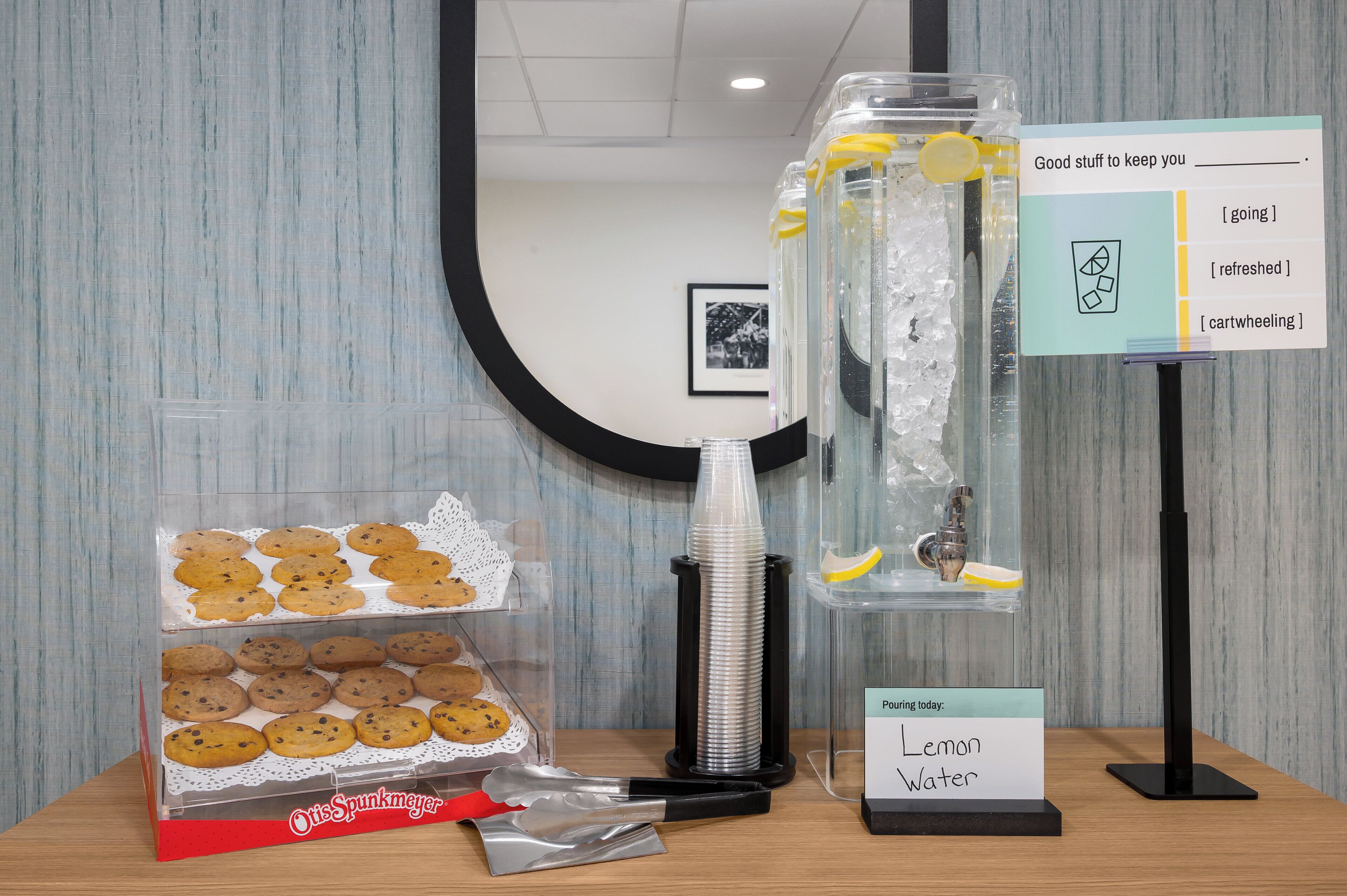 A display of cookies, a lemon water dispenser, and a sign with beverage options.