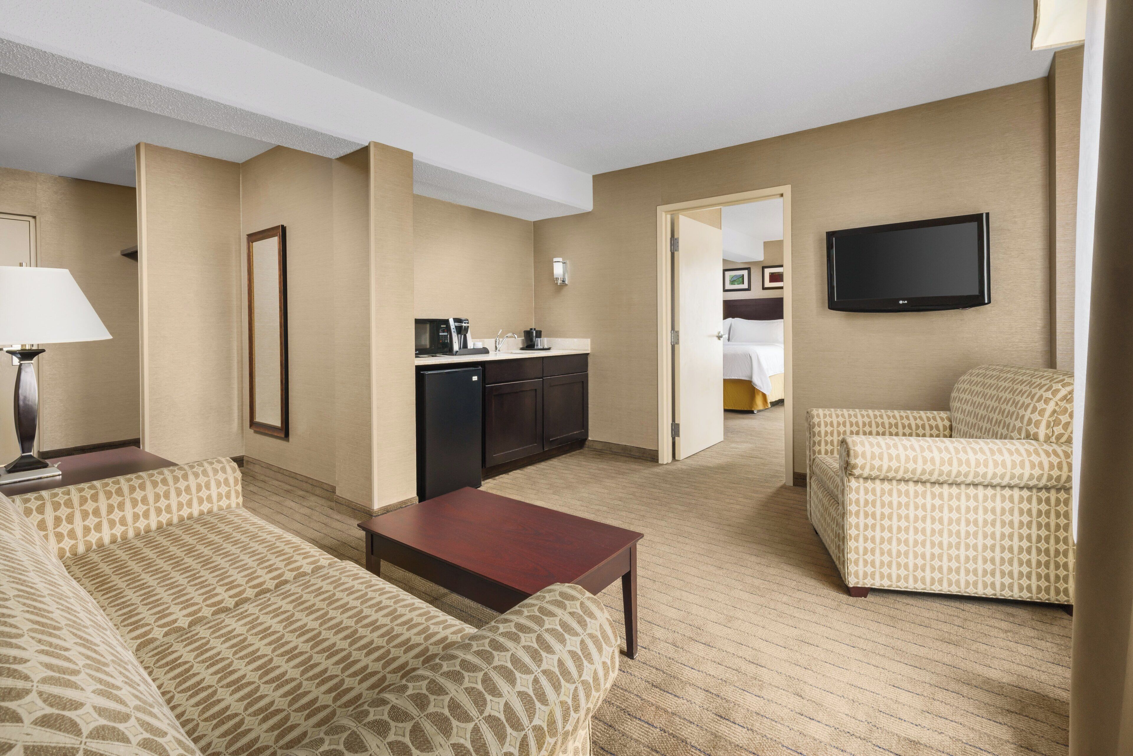 Una habitación de hotel con sala de estar, kitchenette, televisor y cama.