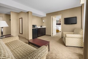 A hotel room with a living area, a kitchenette, a television, and a bed. - Garner Hotel Brockton - Boston by IHG (Brockton)