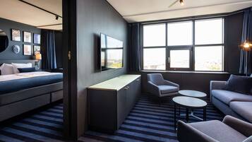 A modern hotel room with a bed, a desk, a sofa, and a TV.
