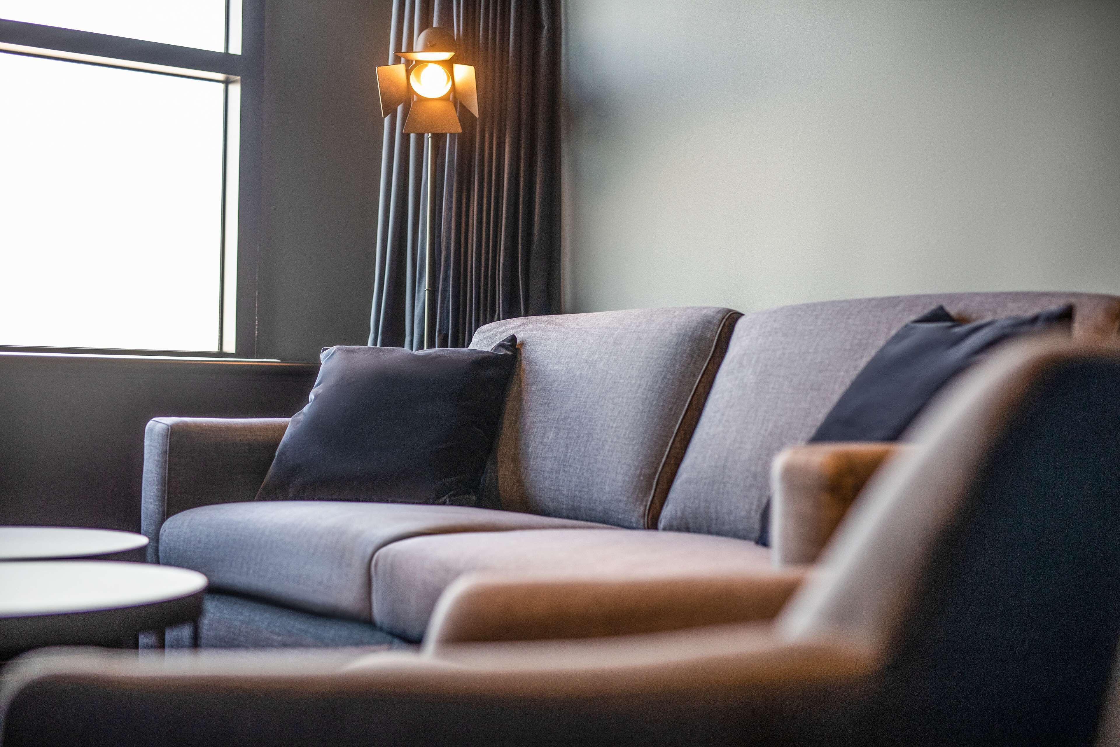 A modern living room with a sofa and armchairs, a small round table, and a floor lamp.