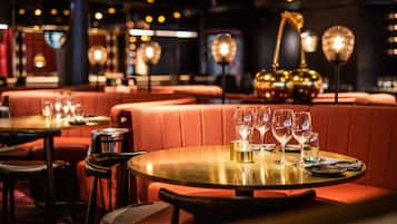 Ein Restaurantinneres mit runden Tischen, rot gepolsterten Sitzecken und hängenden Leuchten.