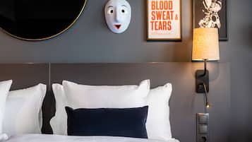 Una habitación de hotel con una cama bien hecha, una lámpara de pared, un cuadro enmarcado y una máscara decorativa.