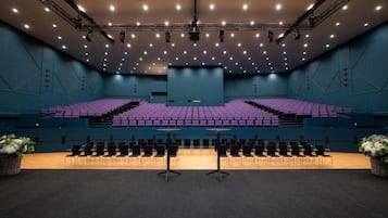 Un auditorio con asientos en niveles, un escenario con un atril y un techo con numerosas luces.