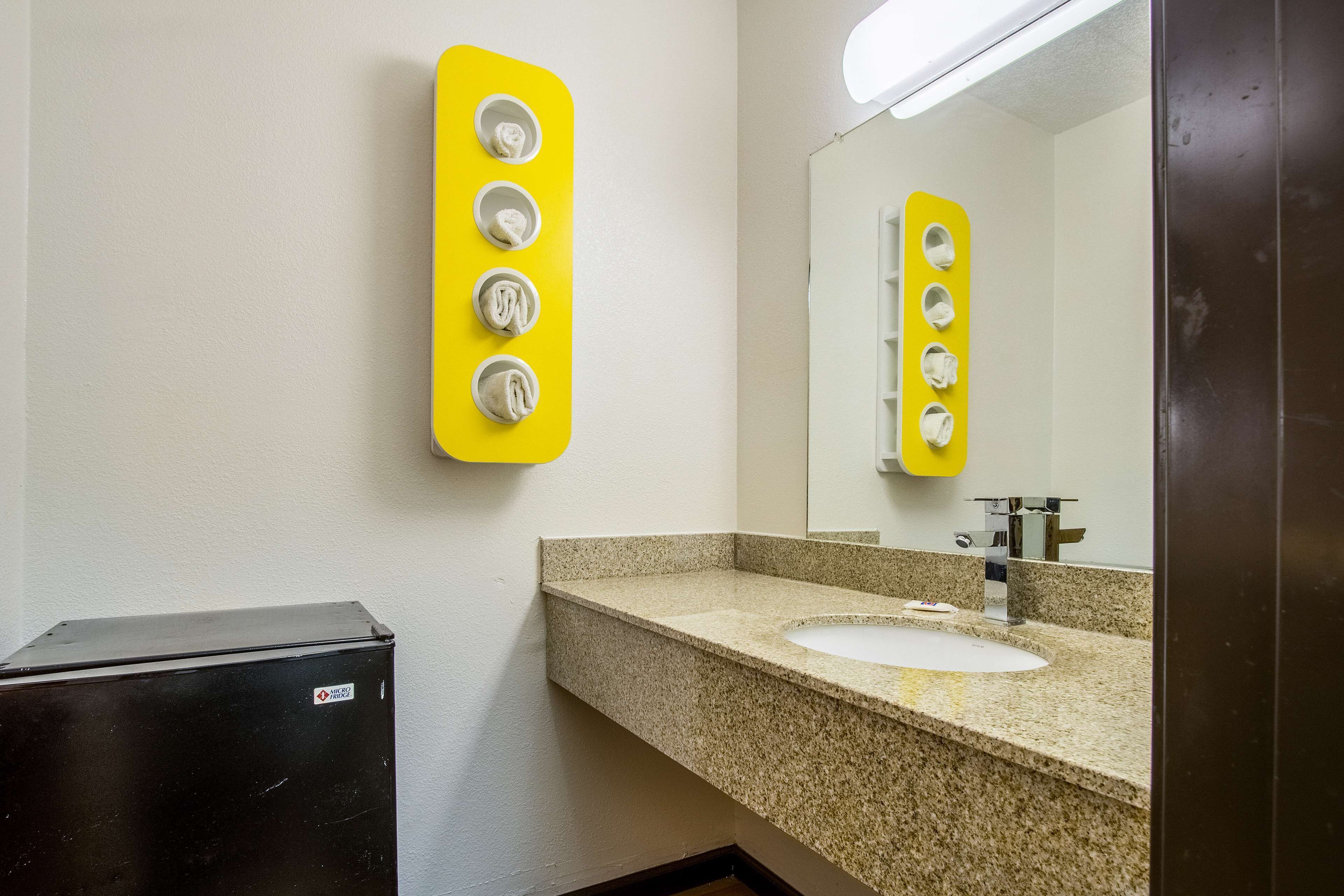 A bathroom with a granite countertop sink, a mirror, and a yellow soap dispenser wall.