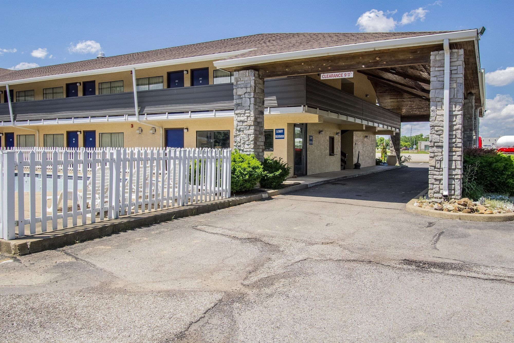 A motel with a covered parking area, a white picket fence, and a stone pillar.