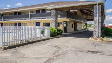 A motel with a covered parking area, a white picket fence, and a stone pillar.