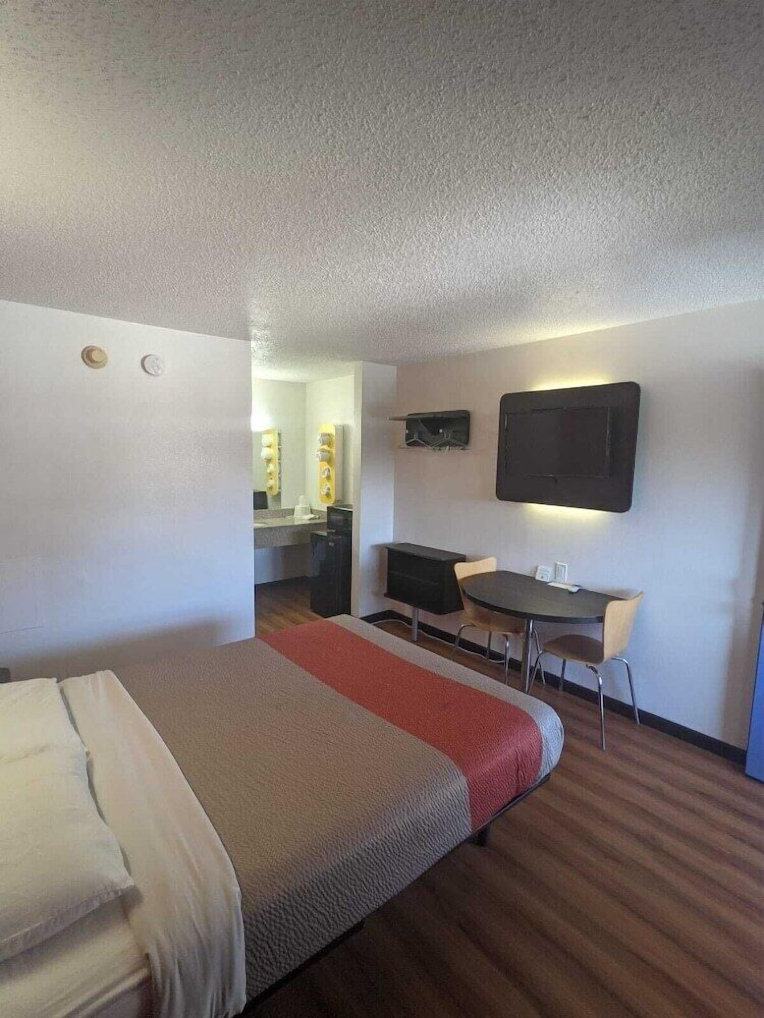 Quarto de hotel com cama, escrivaninha, cadeira, televisão de tela plana e espelho.