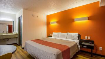 A hotel room with a bed, a bedside table, a nightstand, a mirror, and a bathroom area.