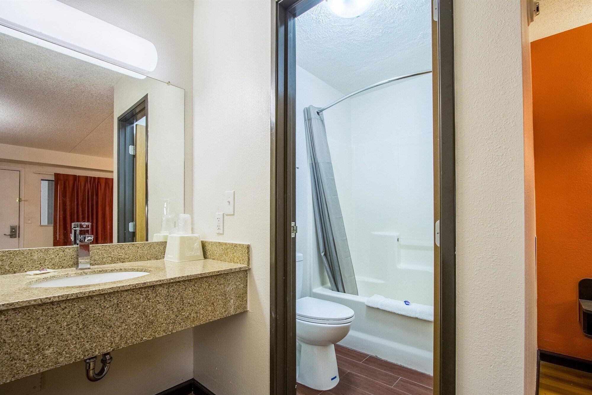 A bathroom with a granite countertop sink, a mirror, a toilet, and a shower area.
