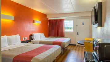 A hotel room with two beds, a television, a microwave, and a window with curtains.