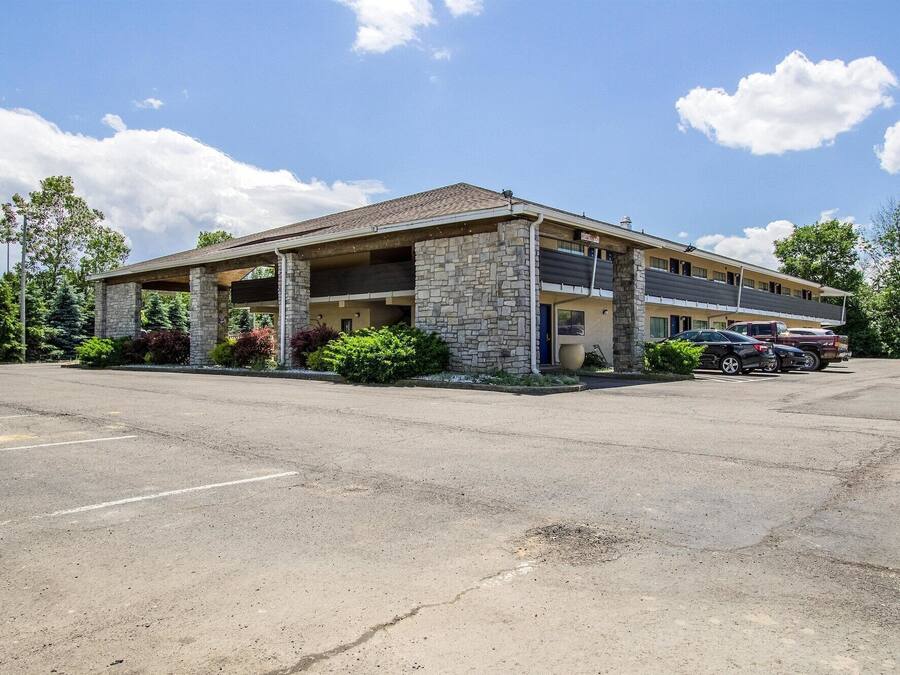 A motel with a stone facade, a covered parking area, and a row of parked cars.