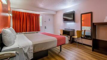 Ein Hotelzimmer mit Bett, Schreibtisch, Stuhl, Fernseher und Spiegel.