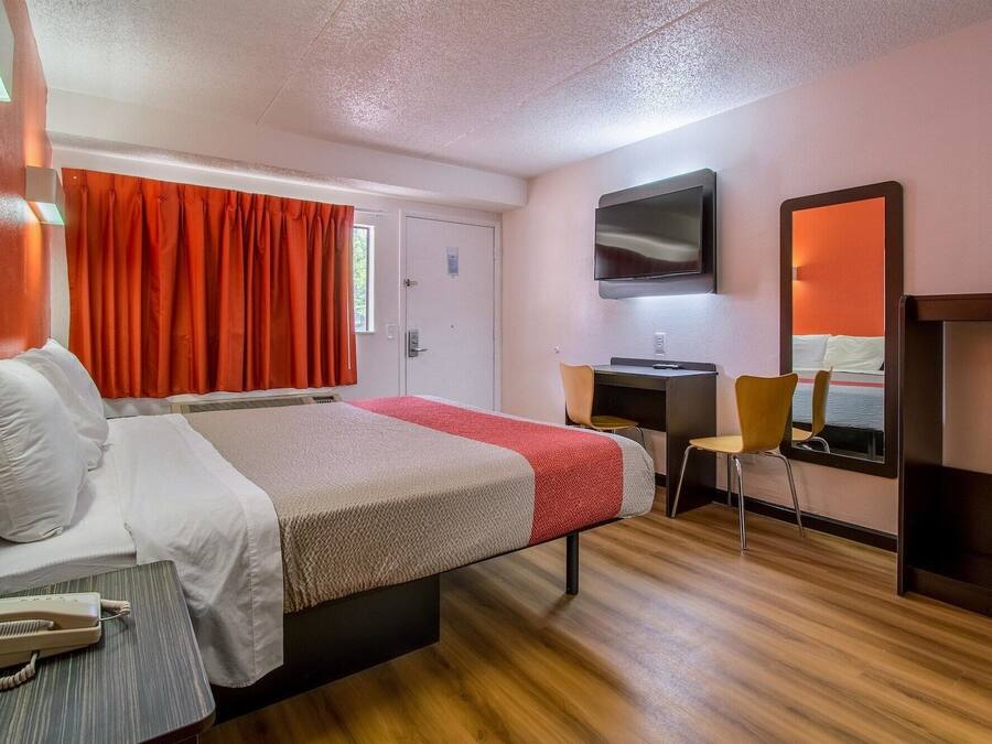 A hotel room with a bed, a desk, a chair, a television, and a mirror.