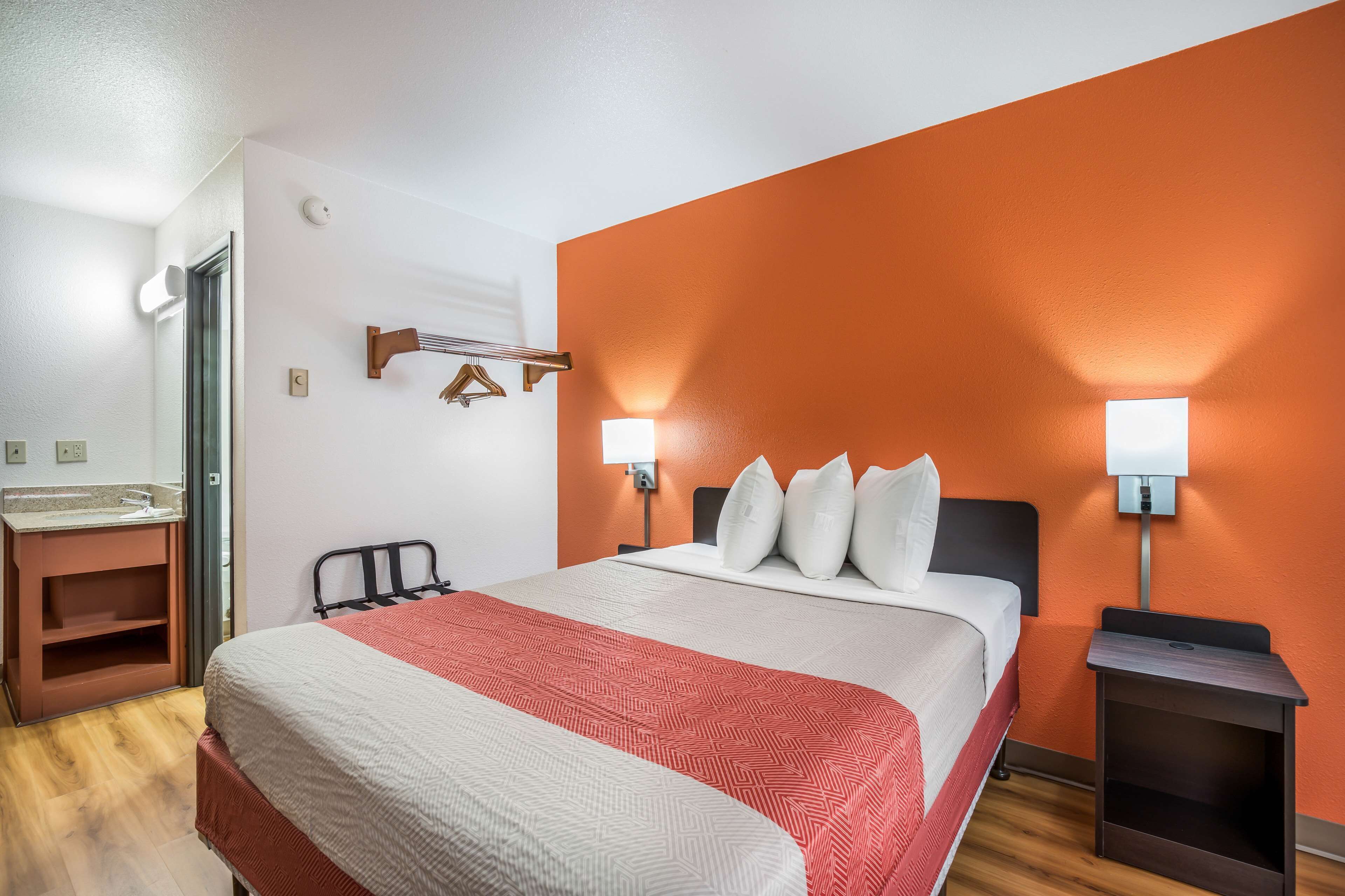A hotel room with a bed, bedside tables, a mirror, and a wooden floor.